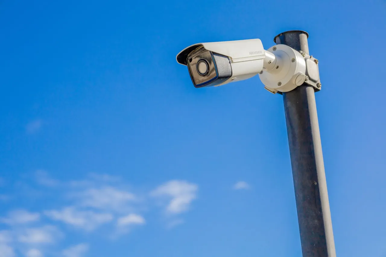 White bullet camera on a black pole against a blue sky
