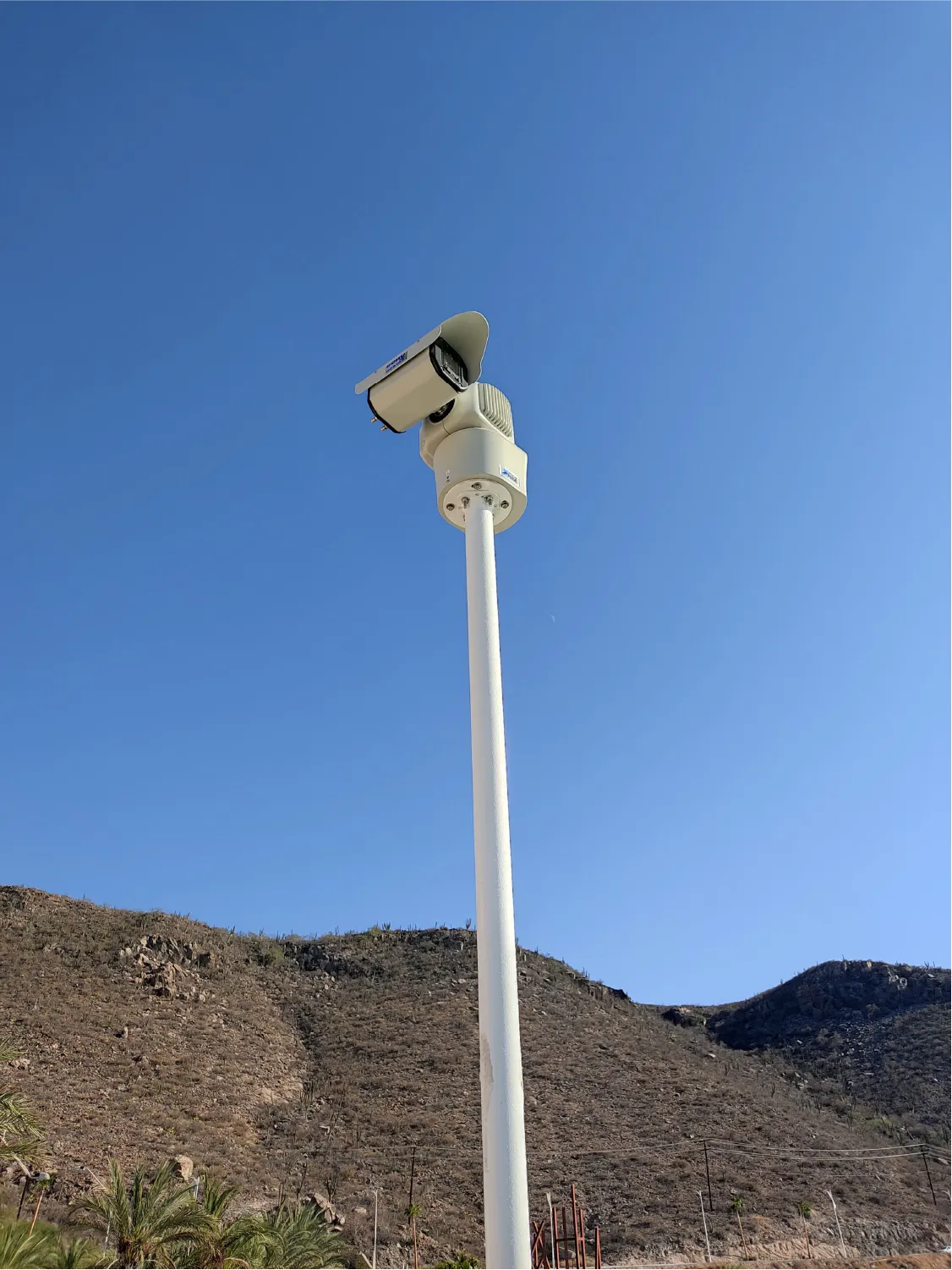 Pan-tilt camera at the top of a white pole, with hills behind