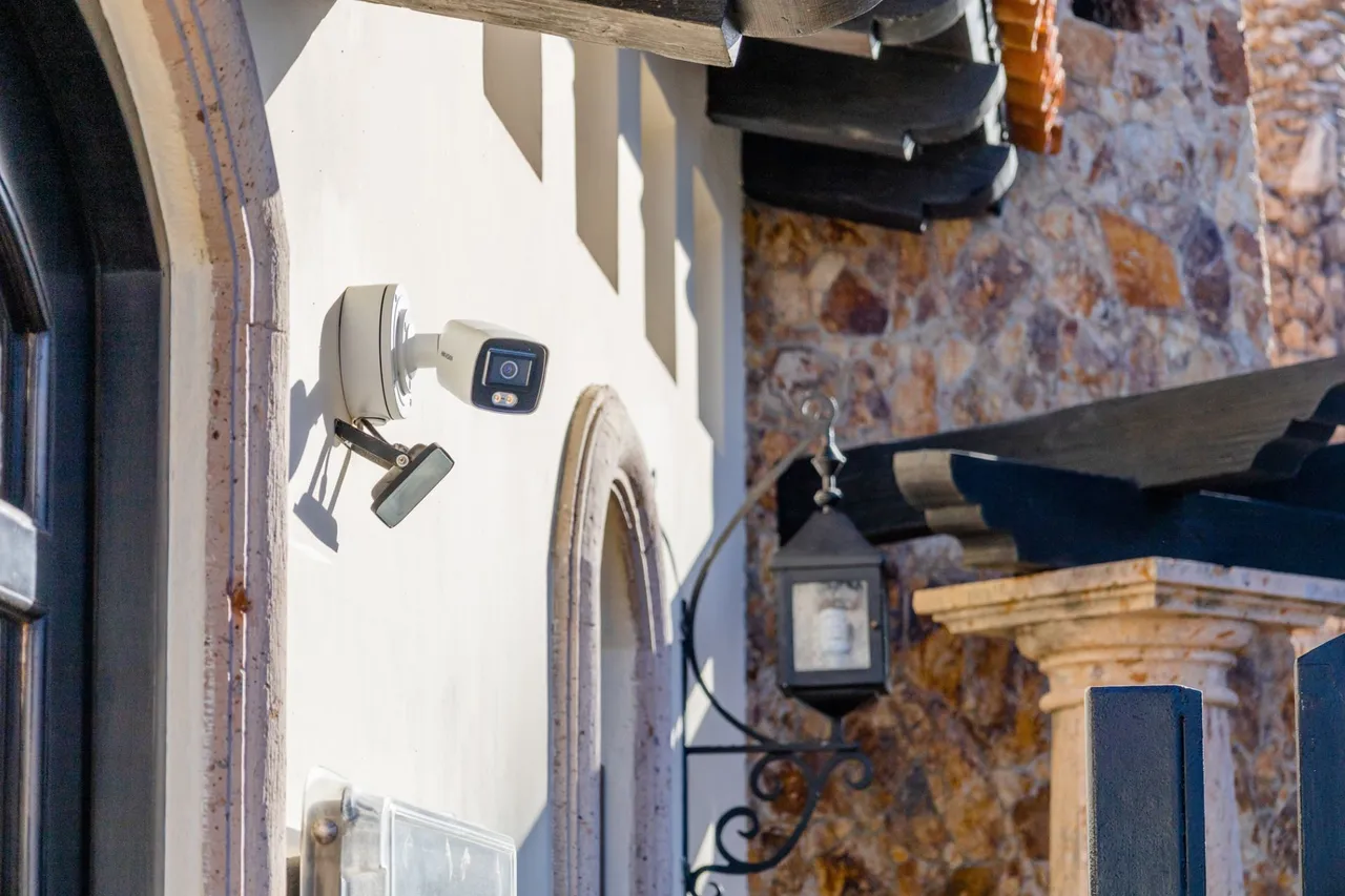 Bullet camera on a stucco wall, beside a stone arch and a wrought-iron lantern