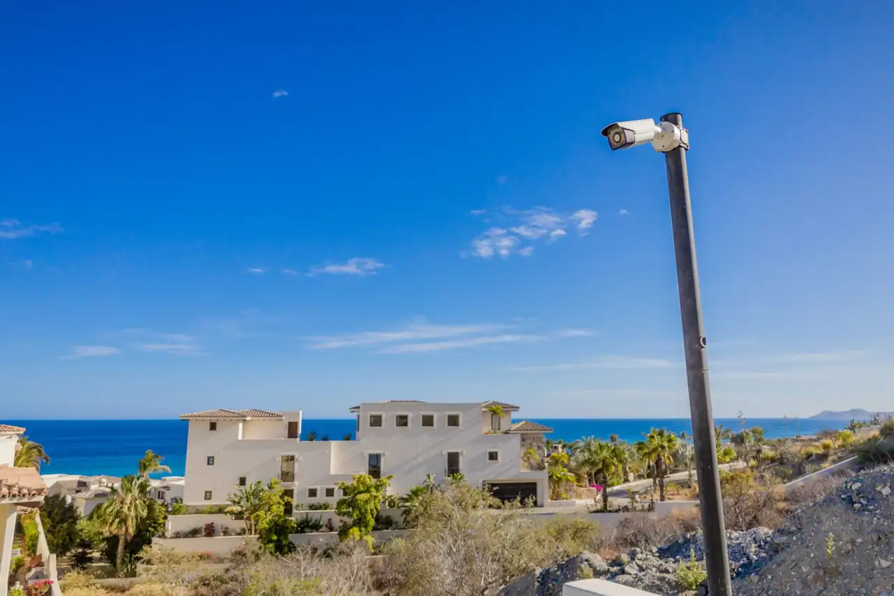 Security camera on a pole with white villas and the ocean in the background