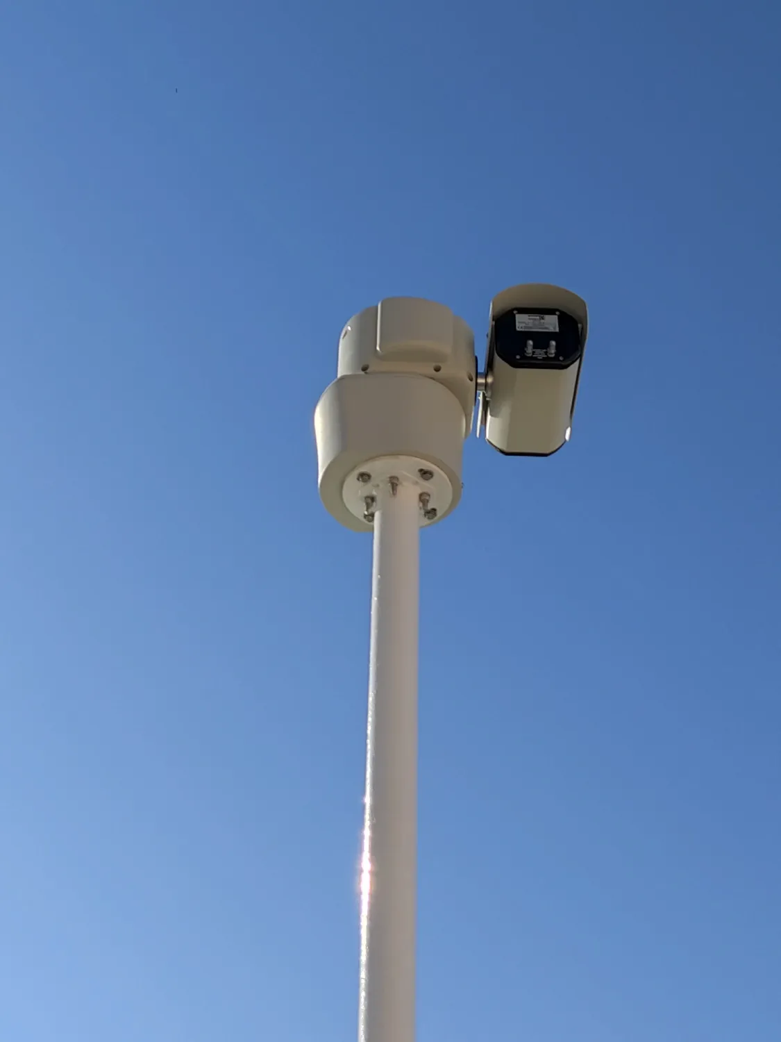 Pan-tilt camera at the top of a white pole, seen from below