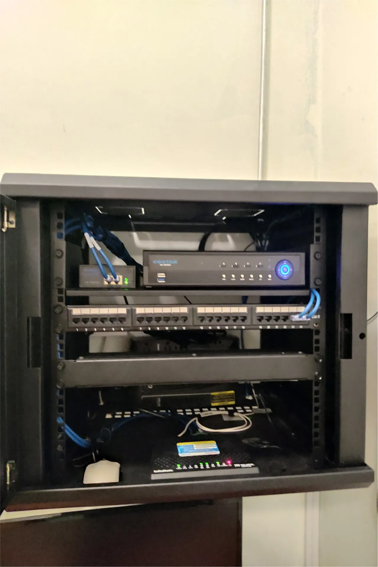 Open wall cabinet with a video recorder, a patch panel and blue cables