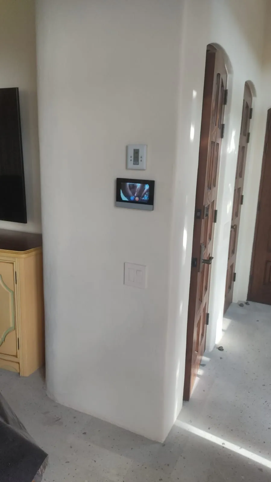 Video intercom monitor on a hallway wall with arched wooden doors