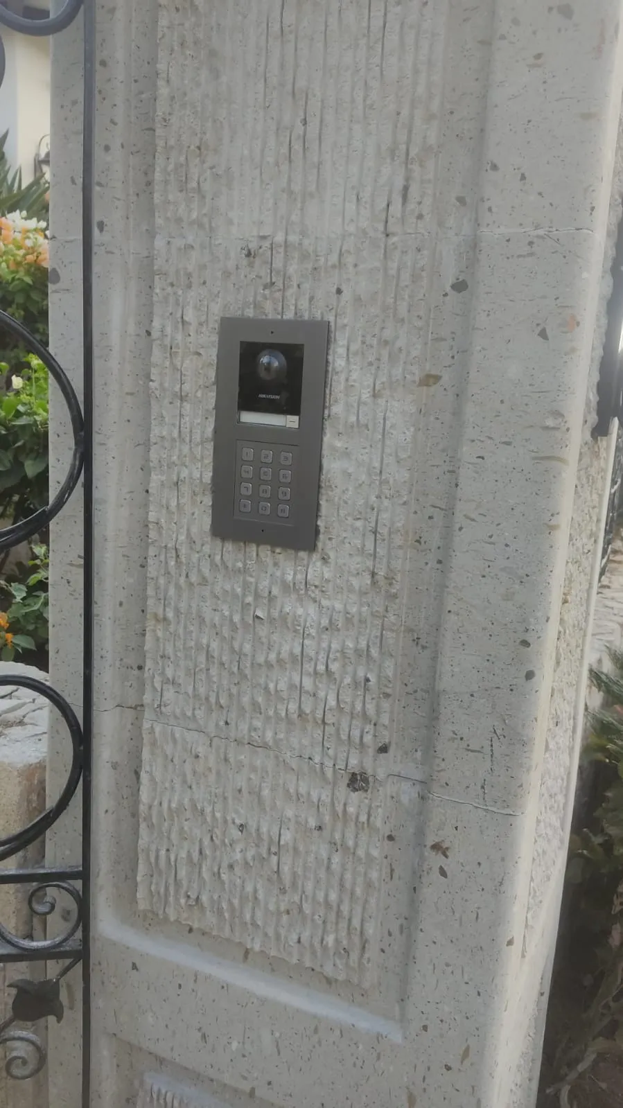 Outdoor video intercom with a keypad on a stone pillar, next to a gate